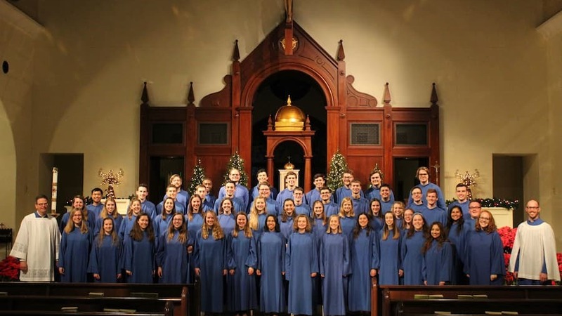 Four rows of choir members in blue robes standing at the front of a church sanctuary.